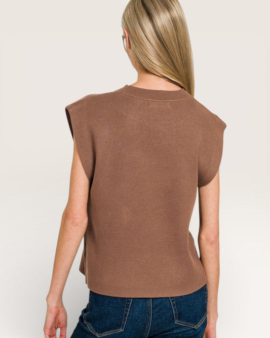 Person wearing a brown sleeveless top and blue jeans on a plain background