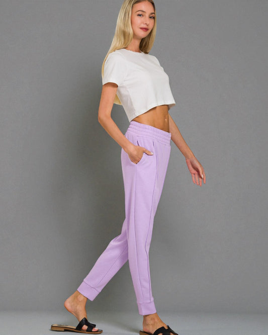 Woman wearing a white crop top and lavender pants against a gray background