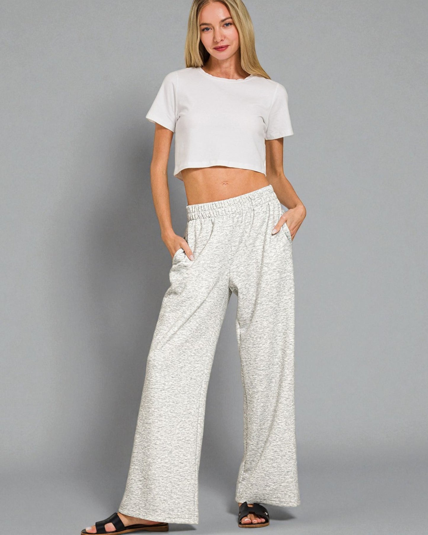 Woman wearing a white crop top and wide-leg pants on a gray background