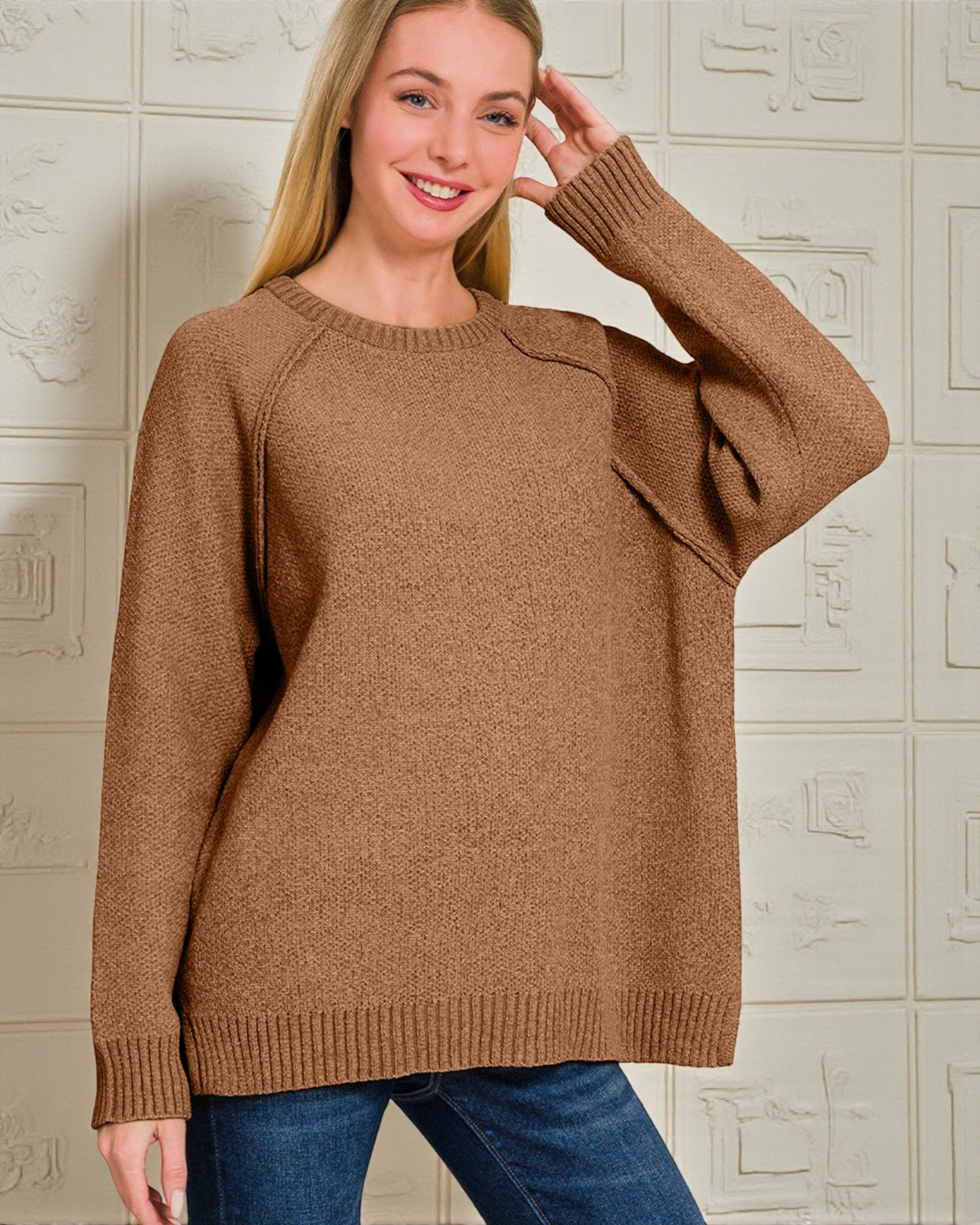Woman wearing a brown sweater against a textured wall.