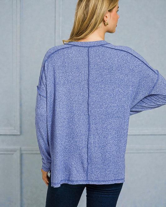 Woman wearing a blue long-sleeve top against a gray wall