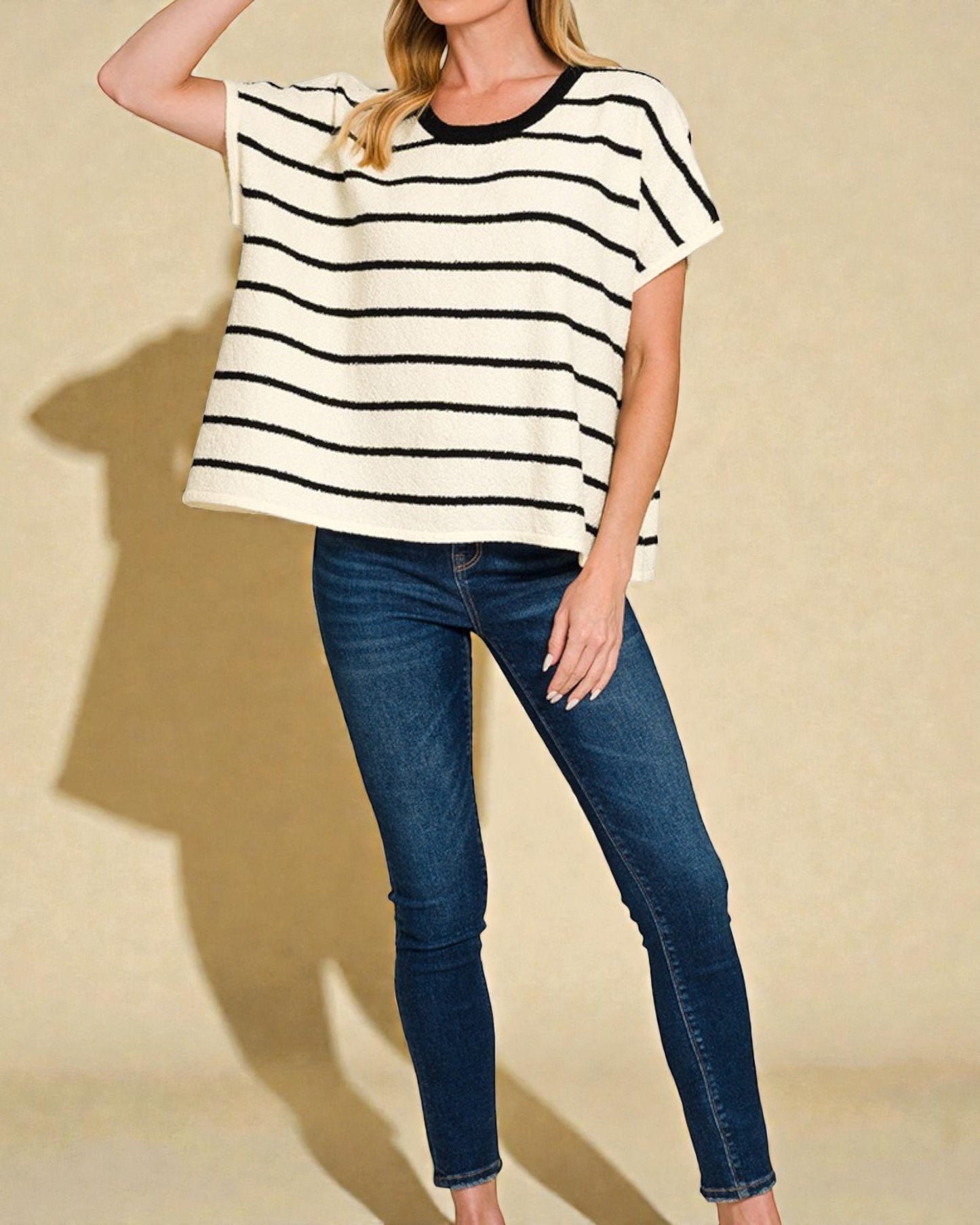 Person wearing a black and white striped shirt and blue jeans on a beige background