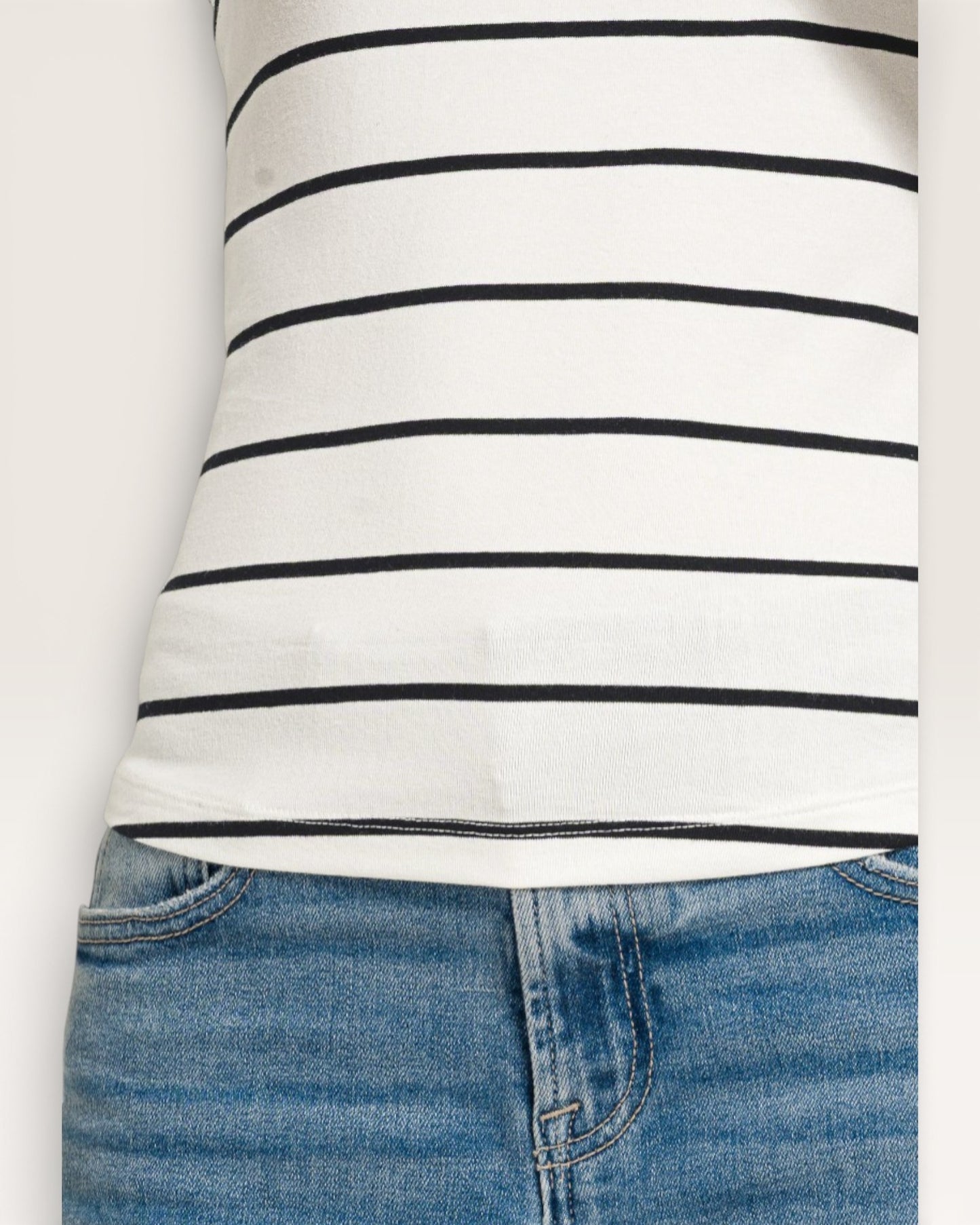 Close-up of a person wearing a white long-sleeve shirt with black stripes and blue jeans on a light gray background.