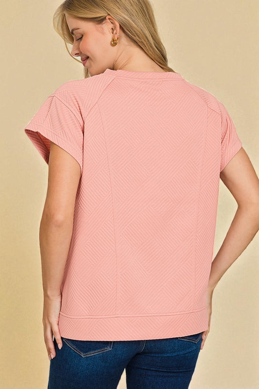 Woman wearing a pink textured top and blue jeans on a beige background