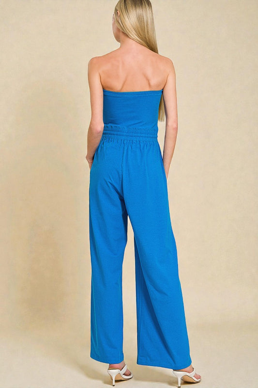 Woman wearing a blue strapless jumpsuit against a beige background