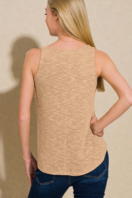 Woman wearing a beige sleeveless top and blue jeans against a plain background