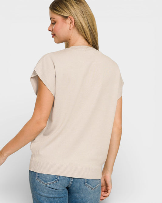 Woman wearing a beige sleeveless top and blue jeans against a white background