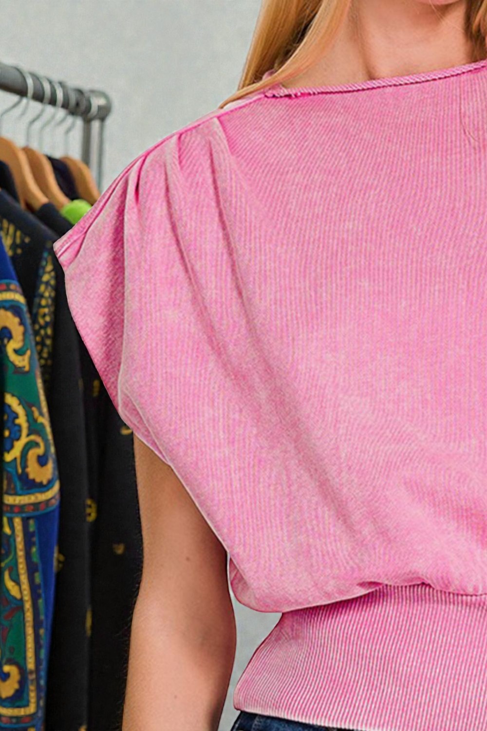 Person wearing a pink top with a rack of clothes in the background