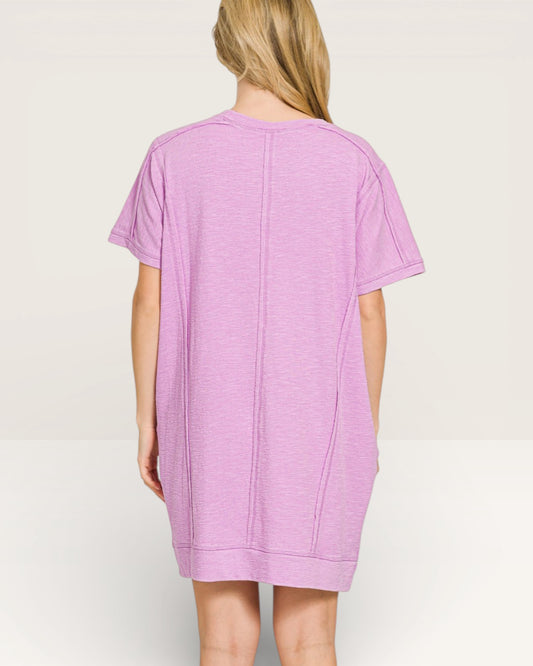 Person wearing a light purple t-shirt dress on a plain background
