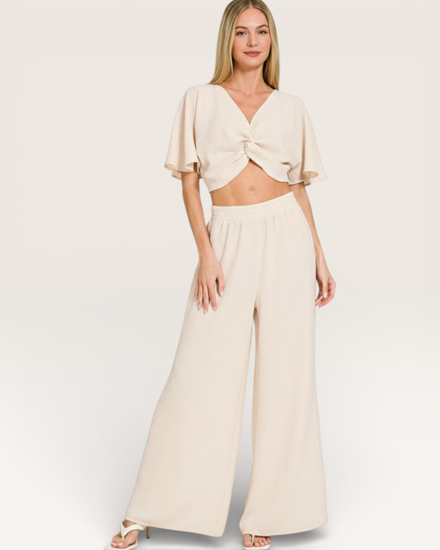 Woman wearing a cream-colored outfit with a top and wide-leg pants on a white background