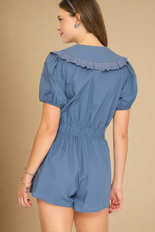 Woman wearing a blue romper with ruffled collar on a light beige background