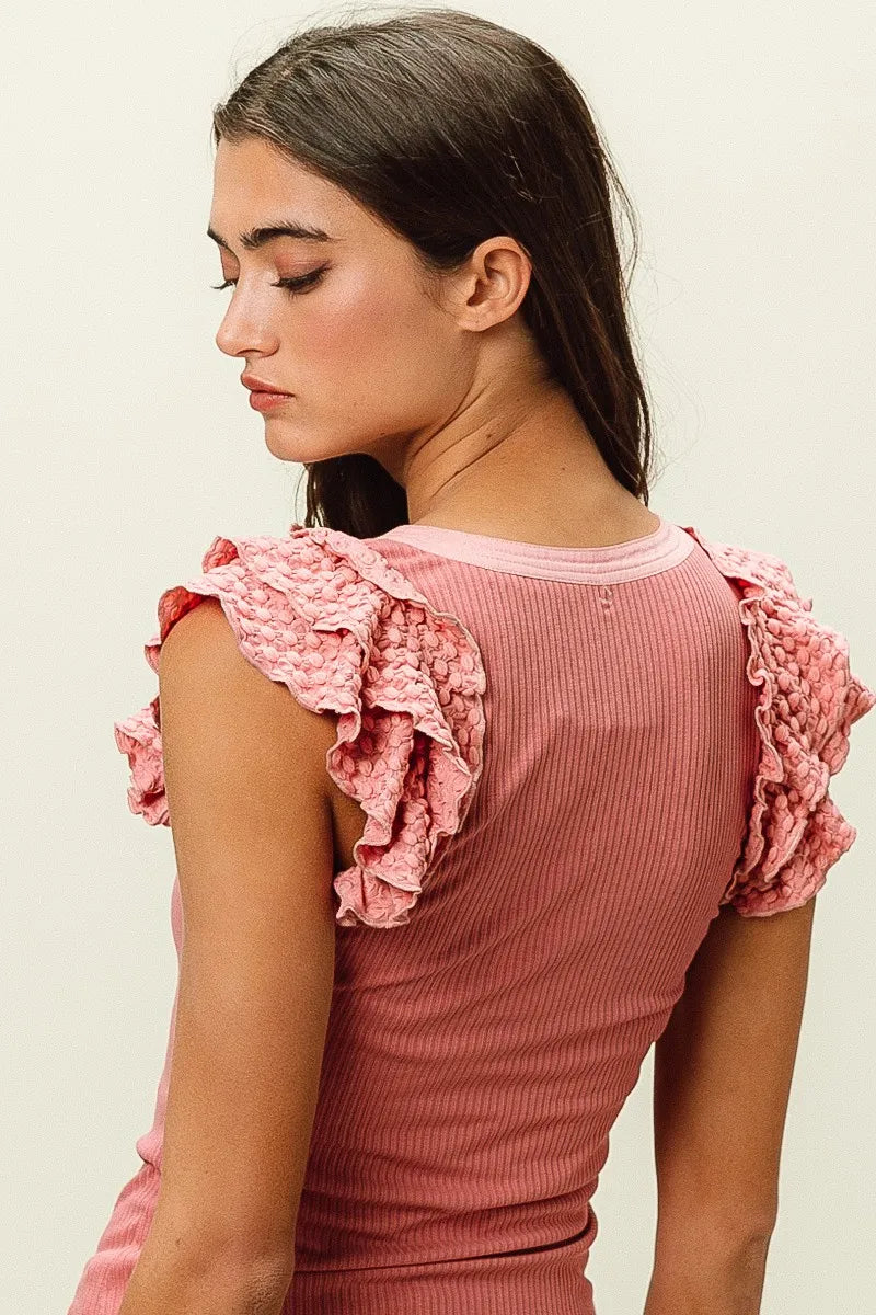 Woman wearing a pink ribbed top with ruffled sleeves on a light background