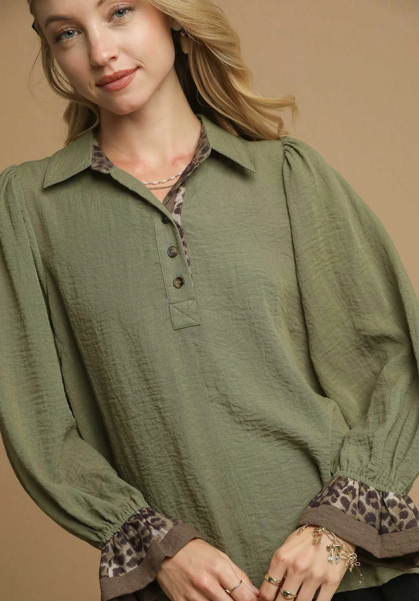 Woman wearing an olive green blouse with leopard print cuffs on a beige background