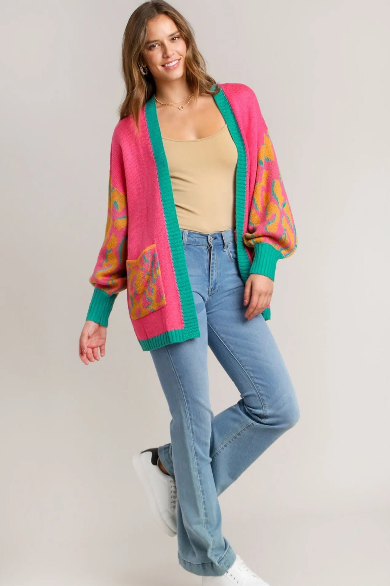 Woman wearing a colorful cardigan, beige top, and blue jeans on a plain background