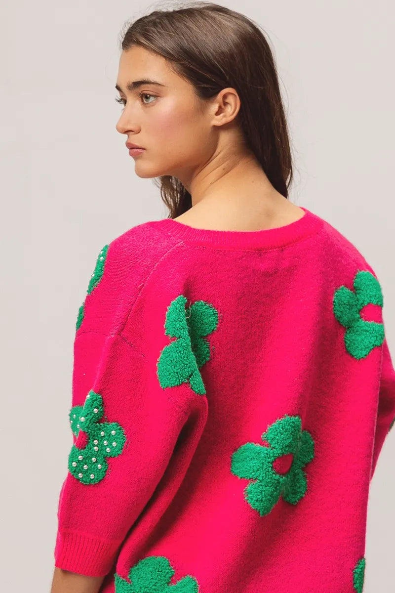 Person wearing a pink sweater with green floral patterns on a plain background