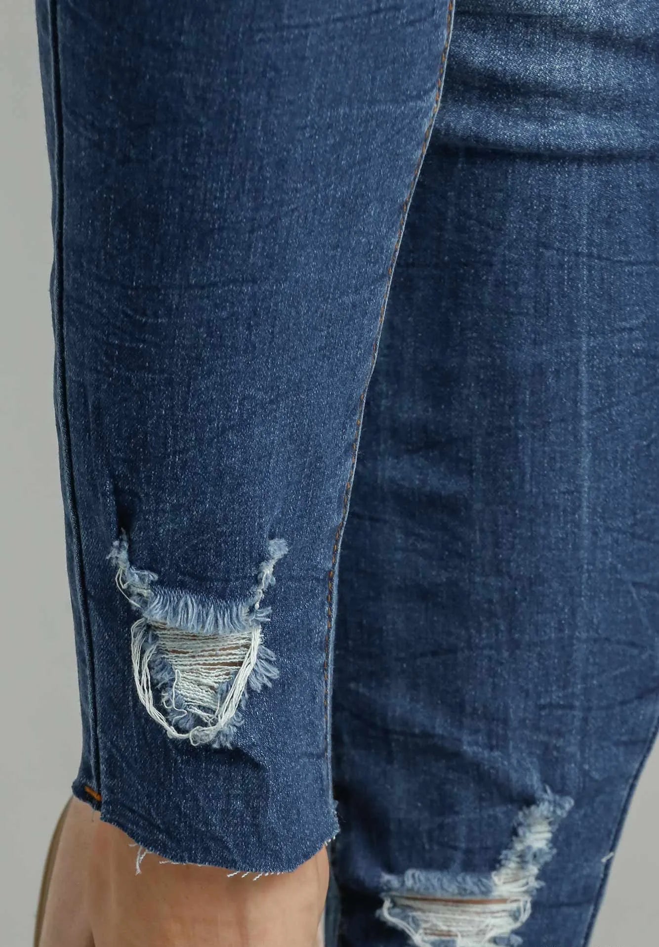Close-up of blue jeans with a frayed hem on a gray background