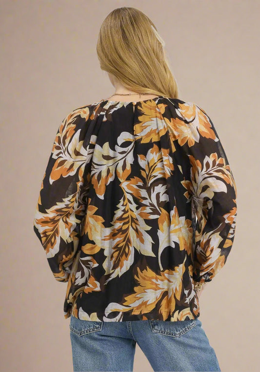 Woman wearing a floral blouse with black, orange, and beige pattern on a beige background