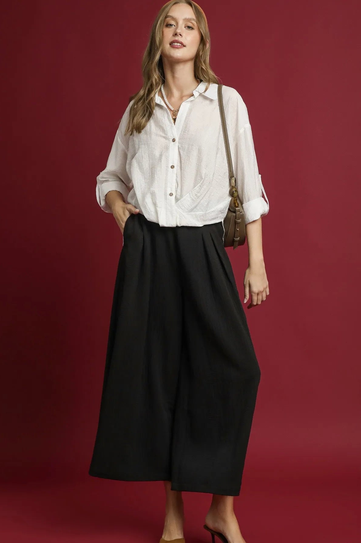 Woman wearing a white shirt and black pants against a red background