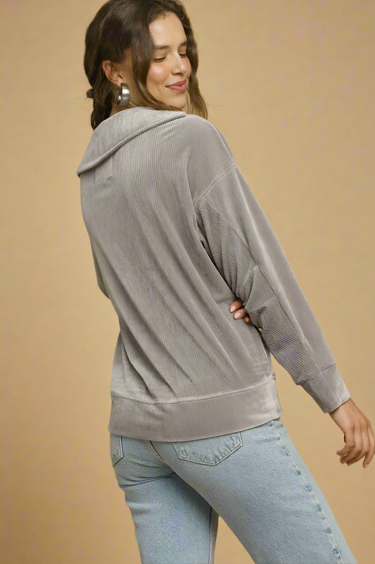 Woman wearing a gray top and light blue jeans against a beige background