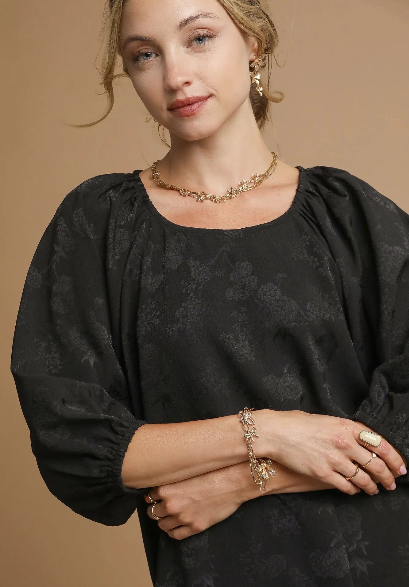 Woman wearing a black top with gold jewelry against a beige background