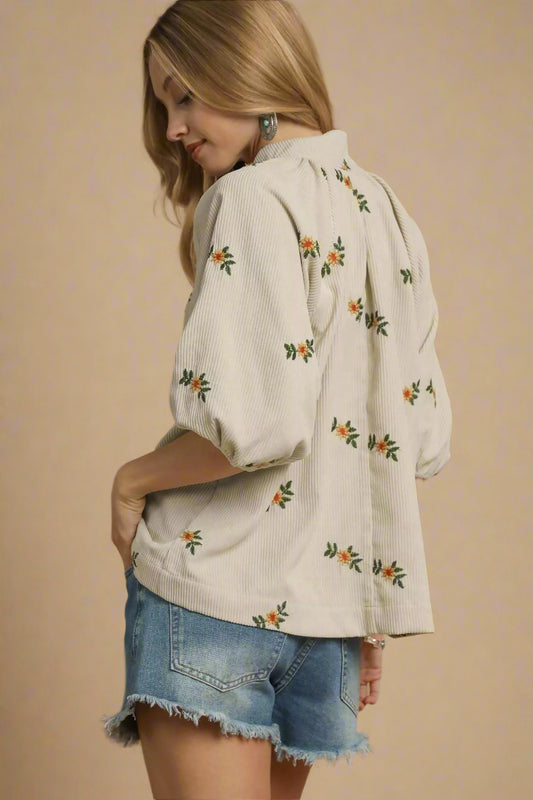 Woman wearing a cream-colored blouse with floral patterns and denim shorts on a beige background