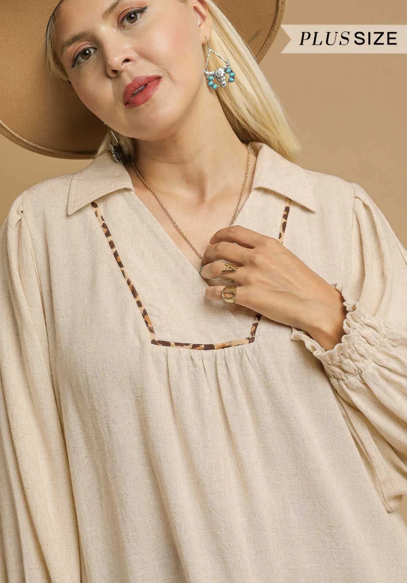 Woman wearing a beige dress with decorative trim, posing against a beige background.