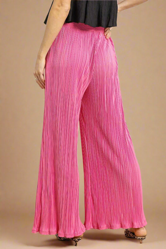 Person wearing bright pink pleated pants on a plain background