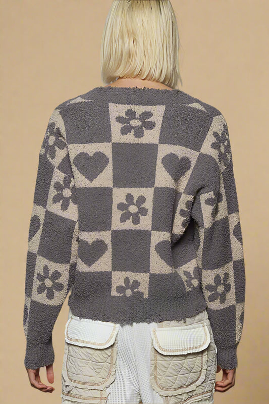 Person wearing a patterned sweater with hearts, flowers, and checkered design against a plain background