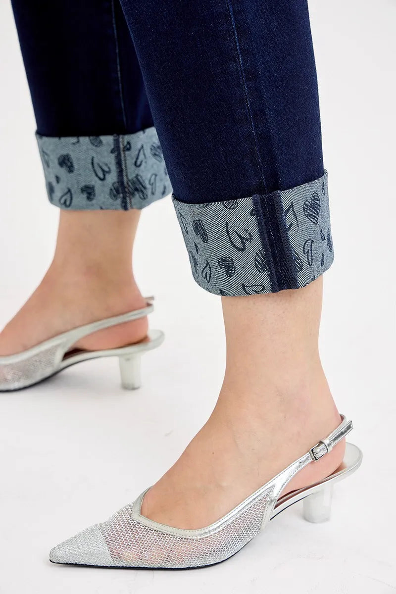 Silver high-heeled shoes worn with rolled-up jeans on a light background