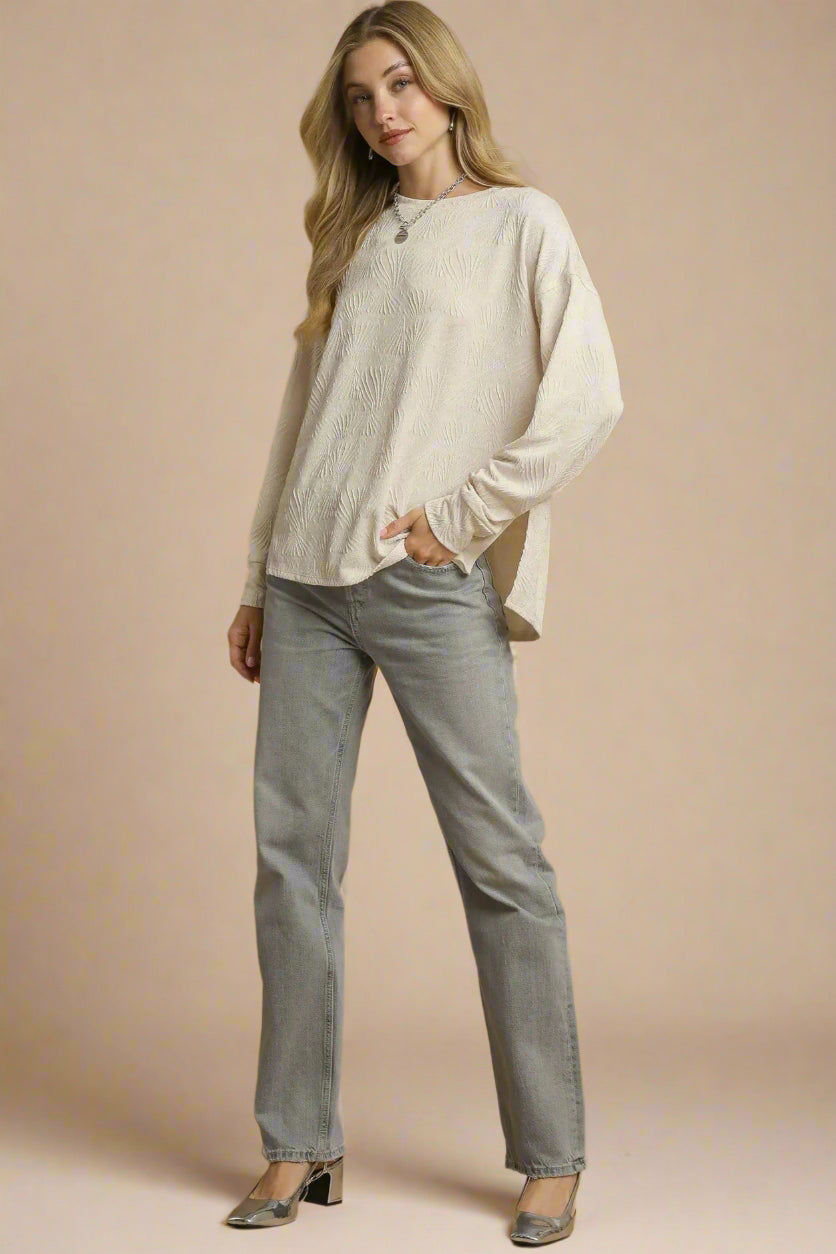 Woman wearing a beige sweater and gray pants against a brown background