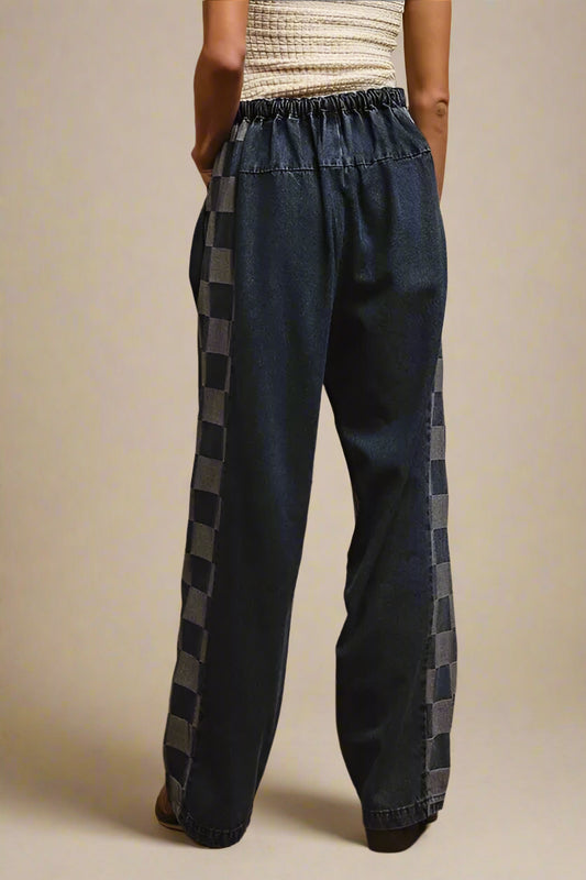 Person wearing blue denim pants with plaid side panels on a beige background