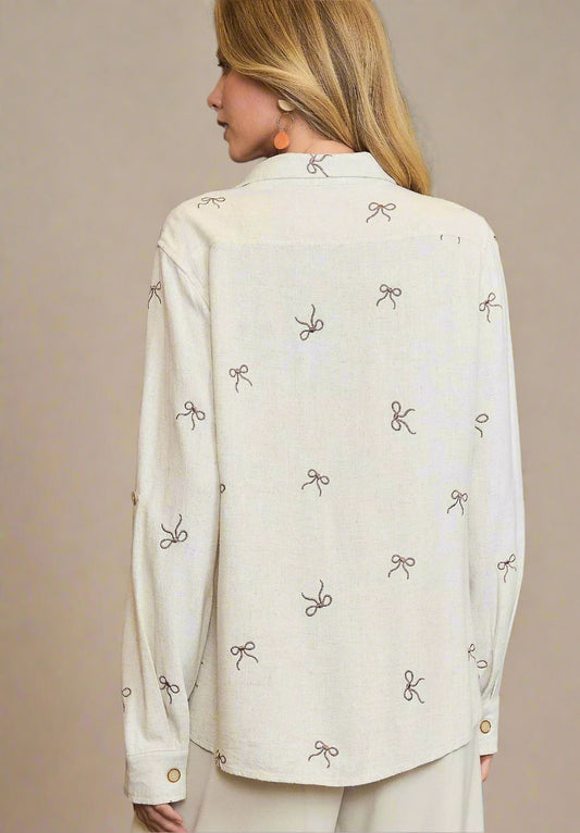 Woman wearing a cream-colored blouse with bow pattern on a gray background