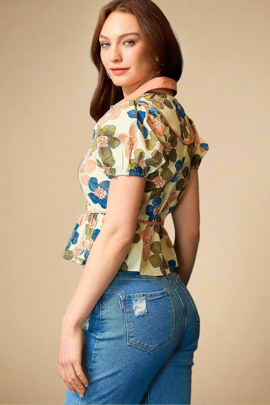 Woman wearing a floral blouse and blue jeans against a beige background