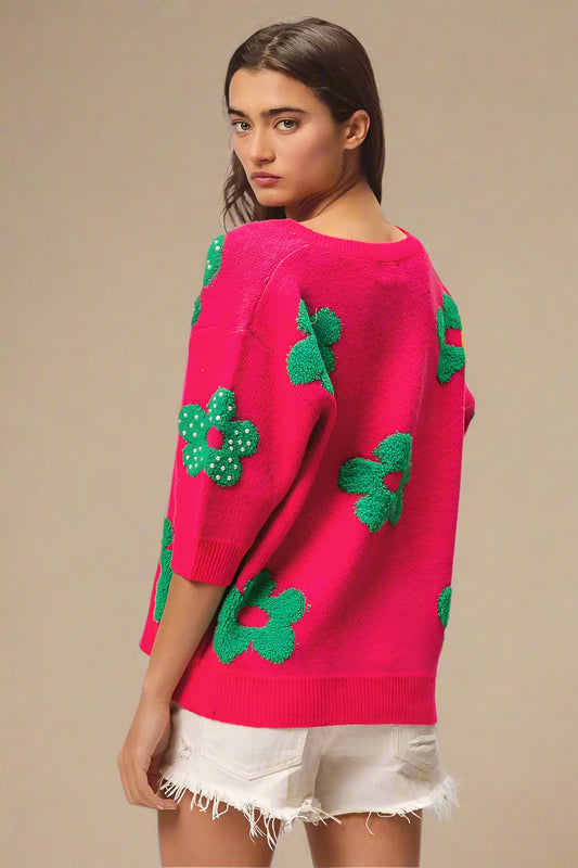 Woman wearing a bright pink sweater with green floral patterns on a plain background