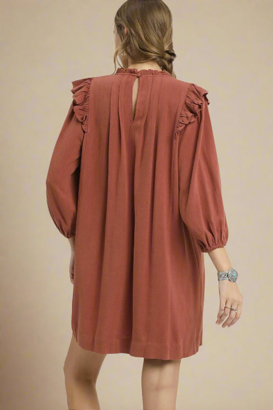 Woman wearing a rust-colored dress with ruffled sleeves on a beige background