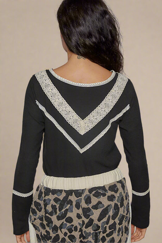 Person wearing a black sweater with white lace details on a beige background