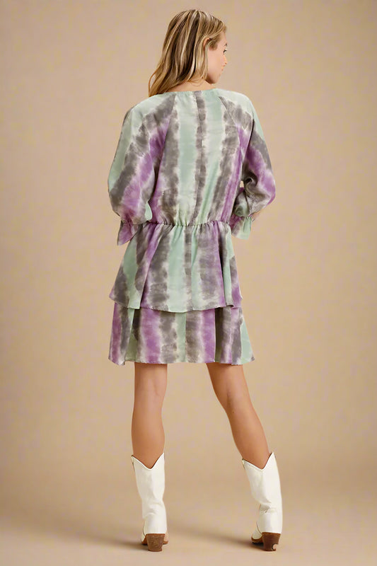 Woman wearing a green and purple tie-dye dress with white boots on a beige background