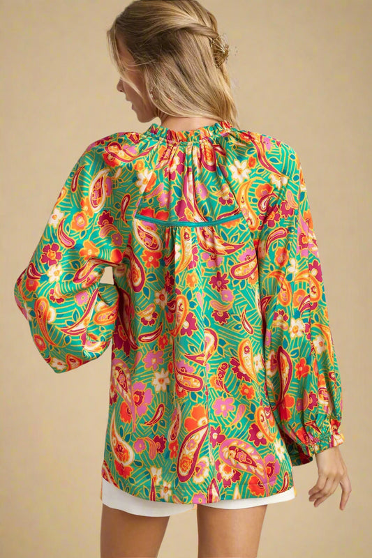 Woman wearing a colorful patterned blouse with long sleeves on a plain background