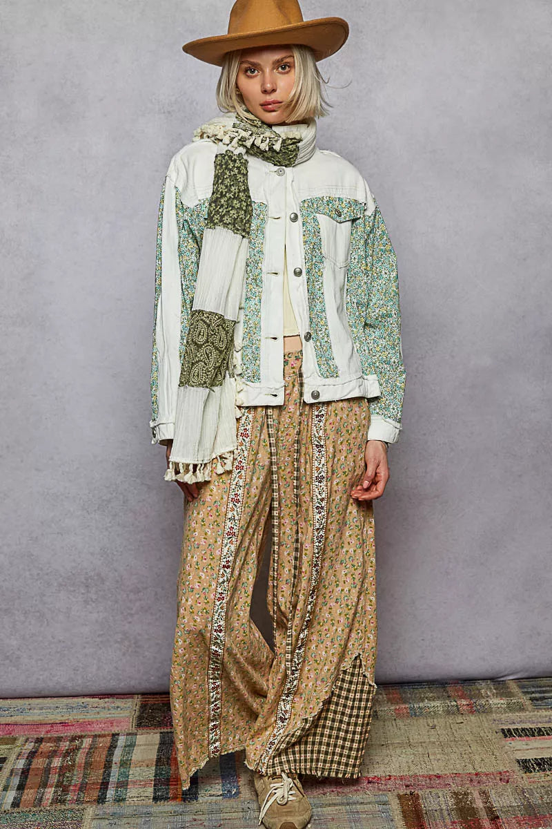 Person wearing a patchwork jacket and patterned pants with a hat against a gray background