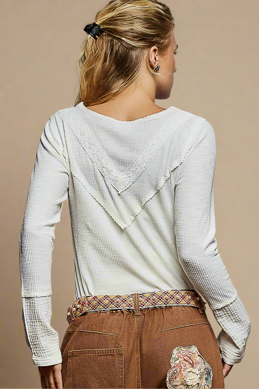 Person wearing a light gray textured long-sleeve top with a decorative back design, standing against a plain background.