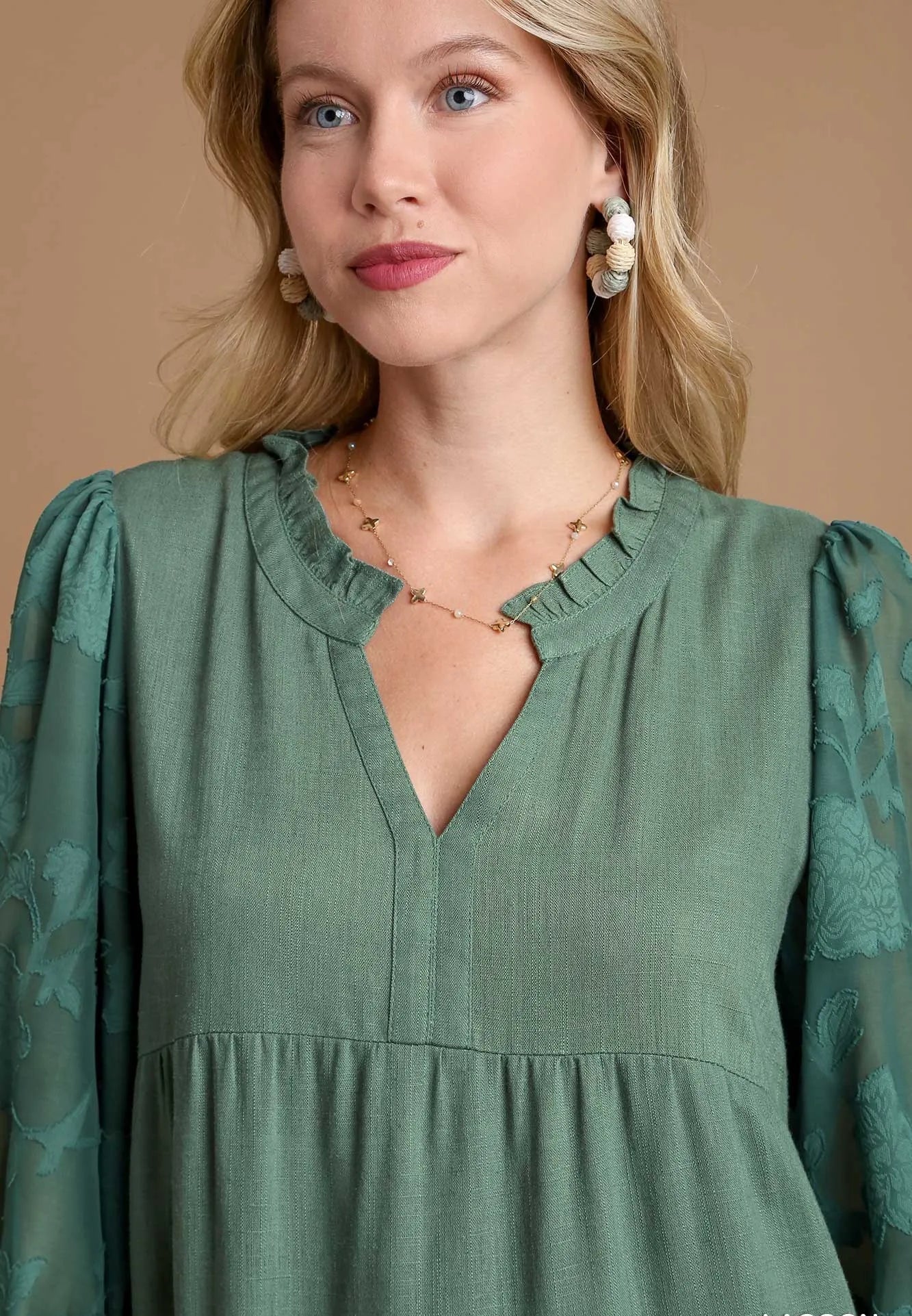 Woman wearing a green dress with floral sleeves against a beige background