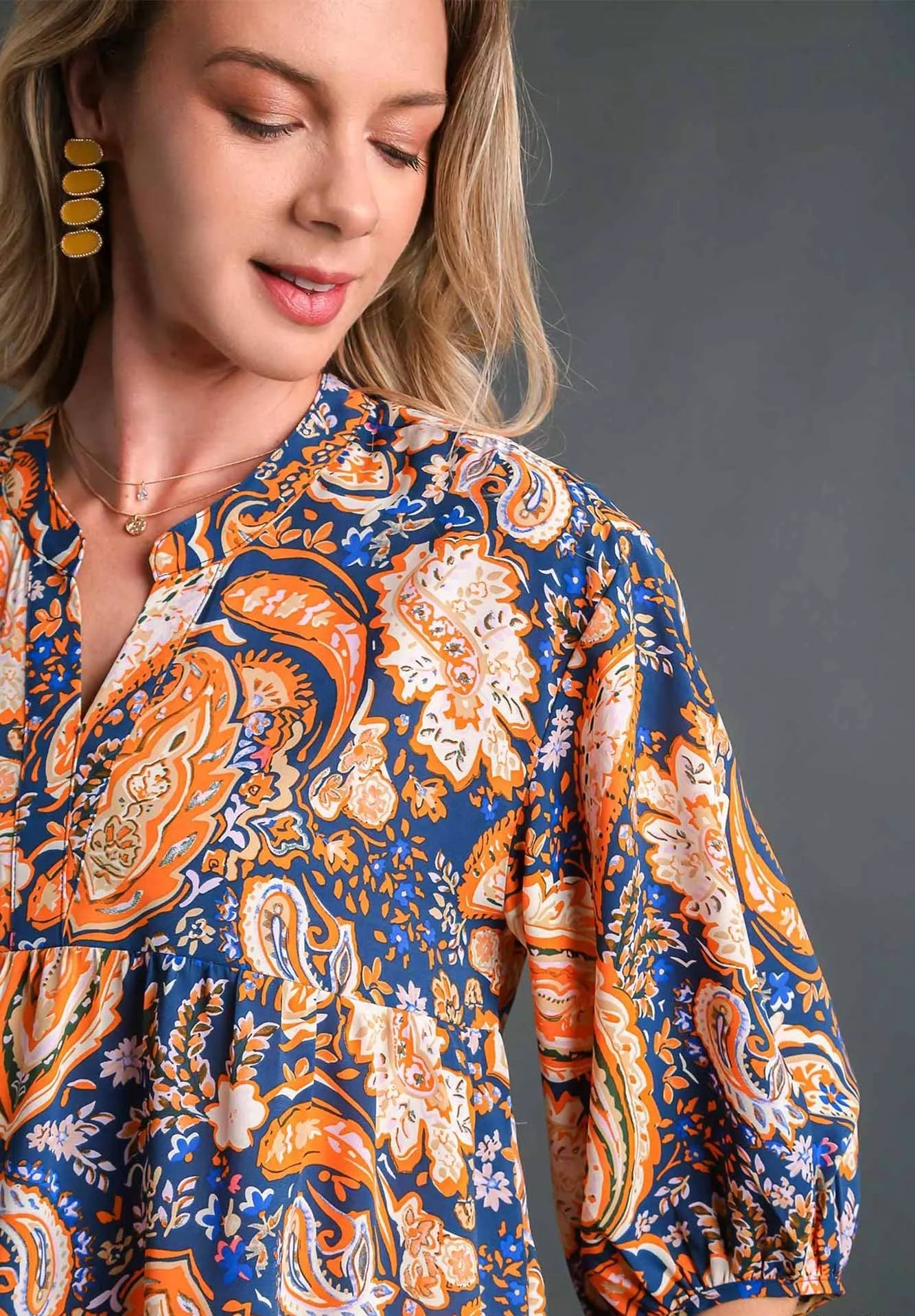 Woman wearing a patterned blouse with orange and blue design on a gray background