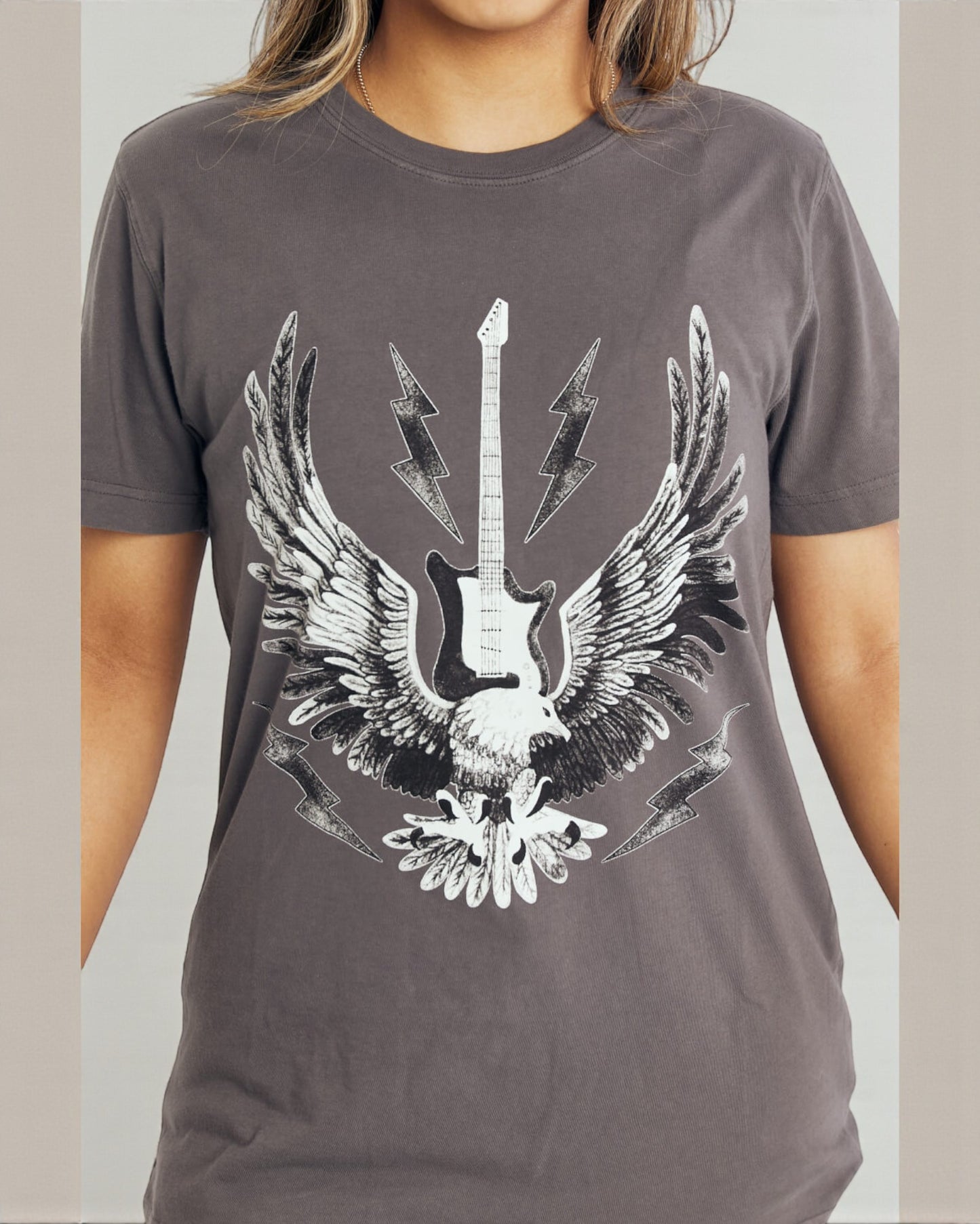 Person wearing a gray t-shirt with a graphic design of an eagle holding a guitar.