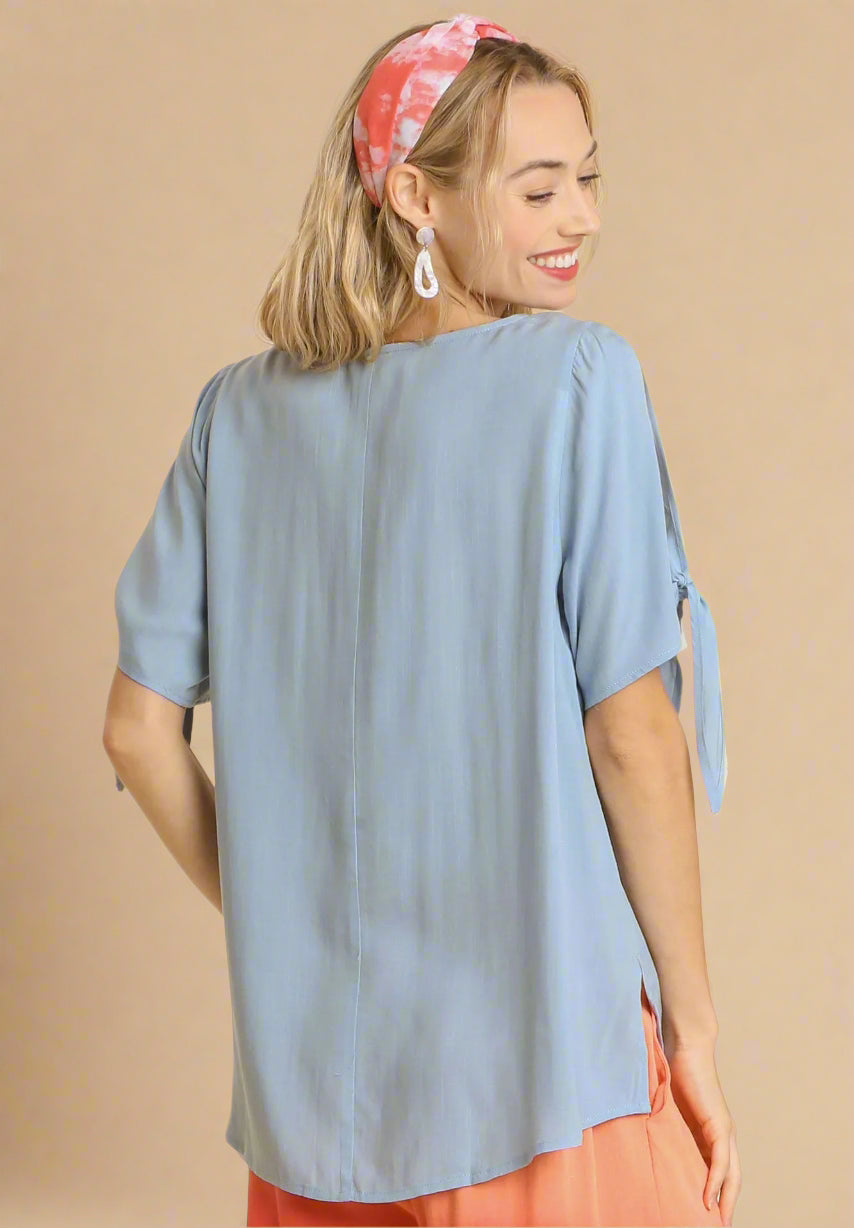Woman wearing a dusty blue top with tied sleeves on a beige background