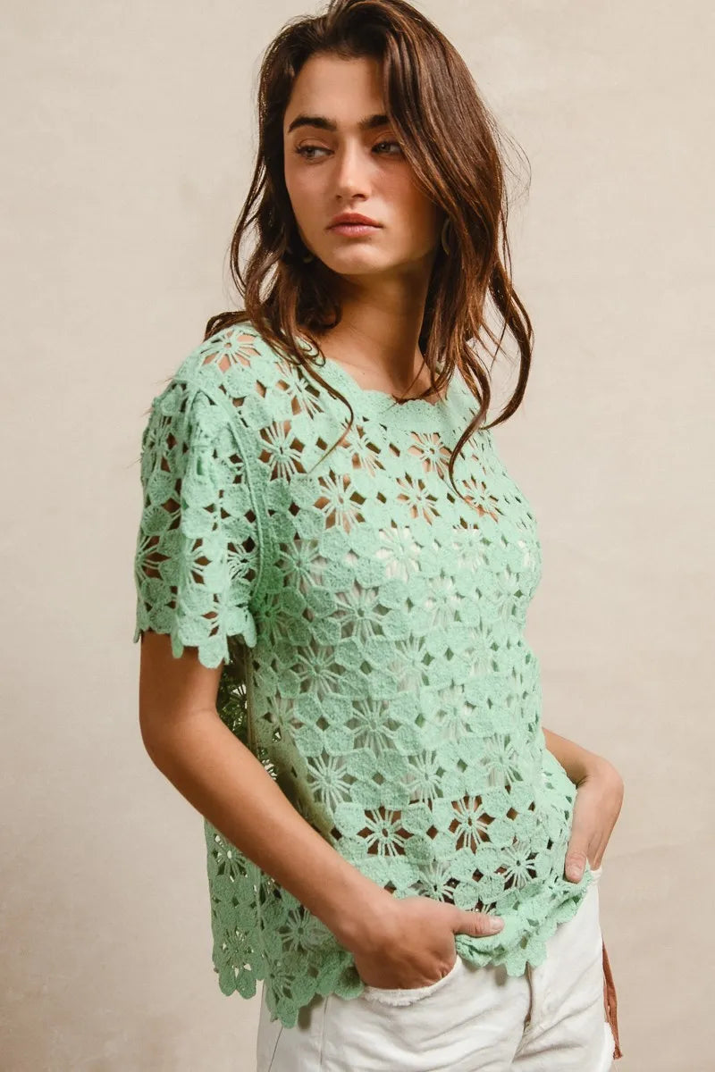 Woman wearing a light green crochet top against a beige background