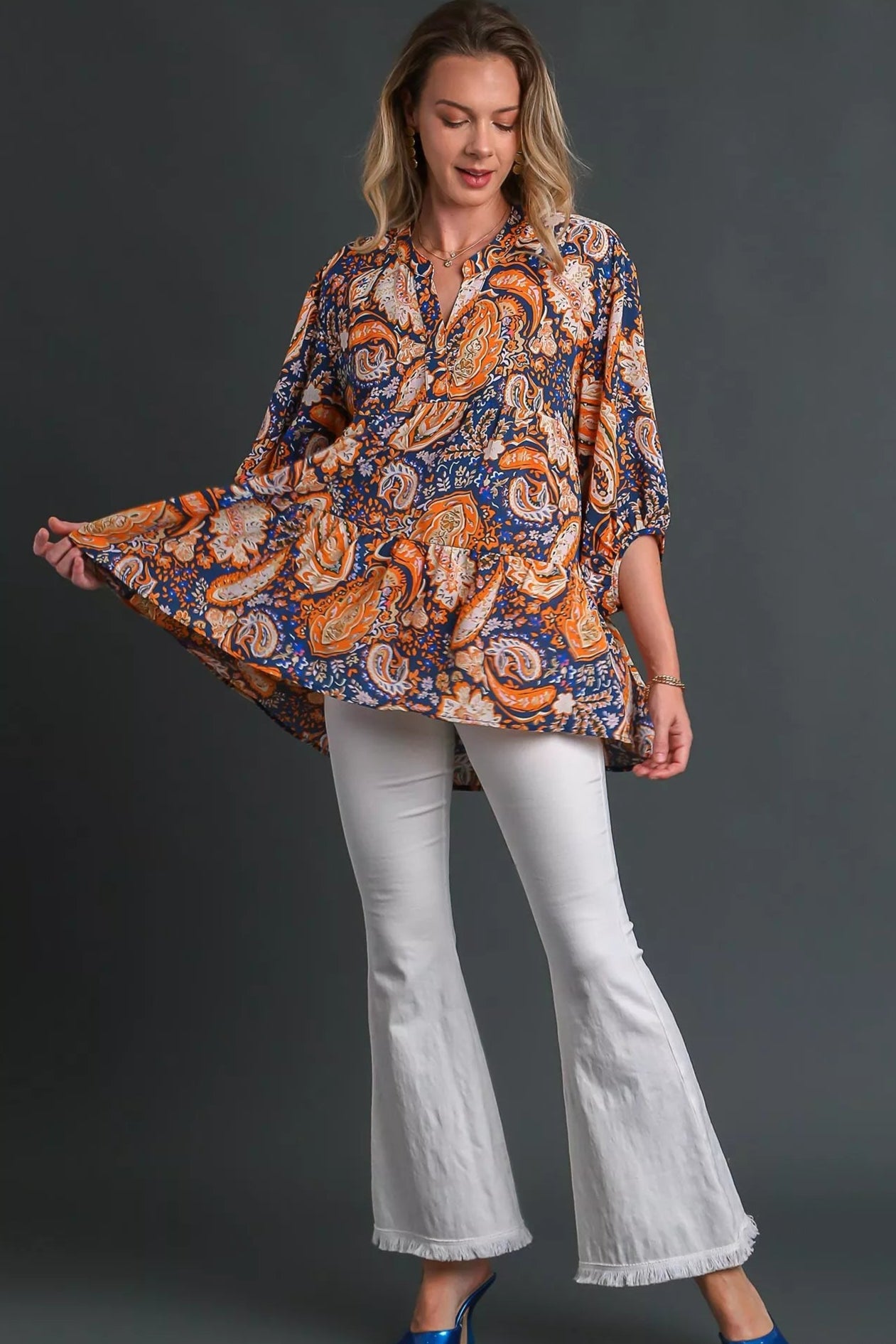 Woman wearing a patterned blouse and white pants on a gray background