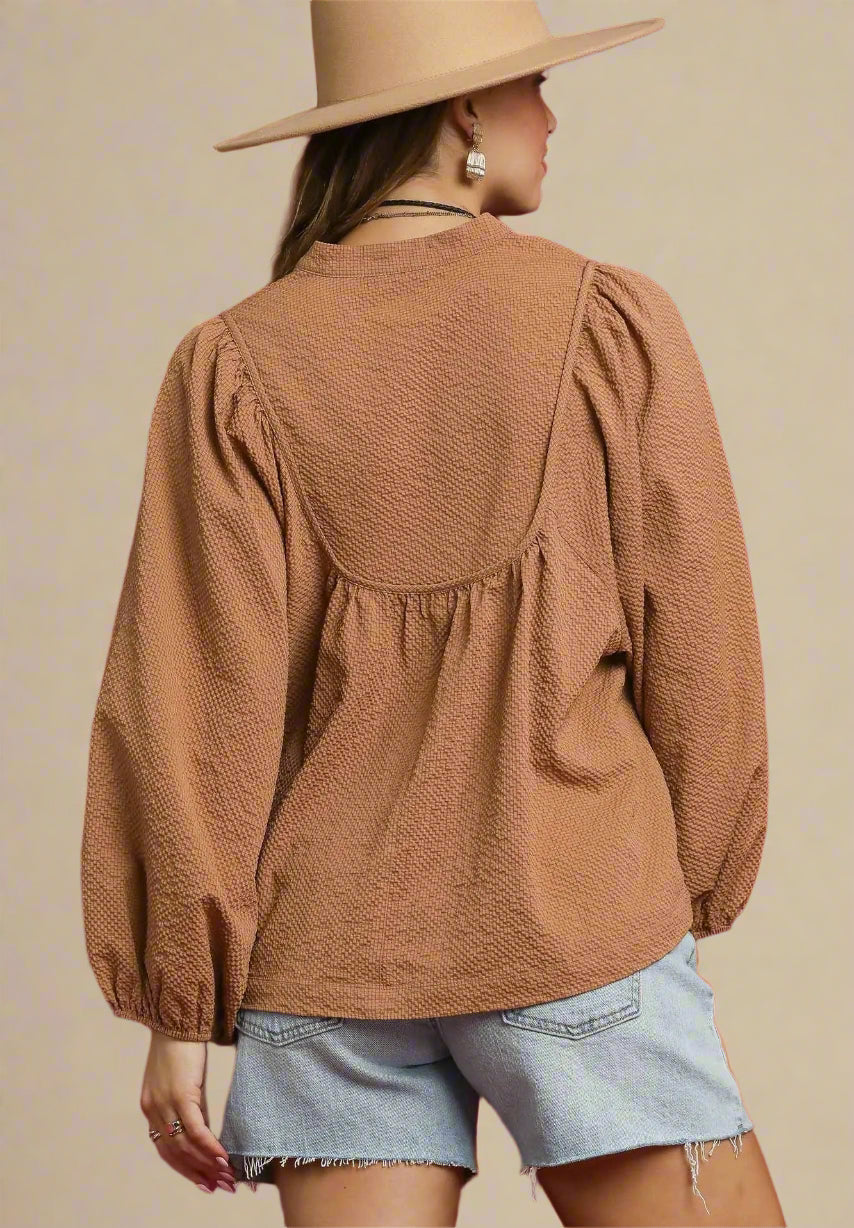 Person wearing a brown textured blouse and denim shorts against a beige background