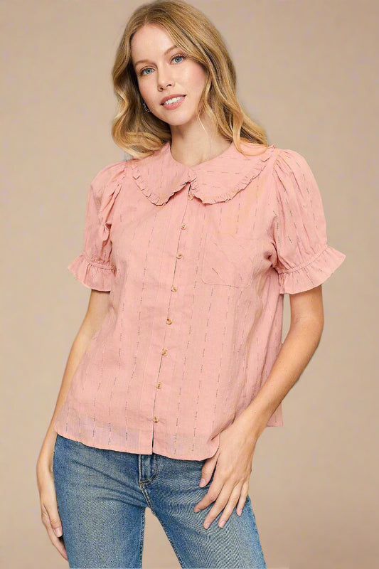 Woman wearing a pink blouse with ruffled sleeves and collar against a beige background