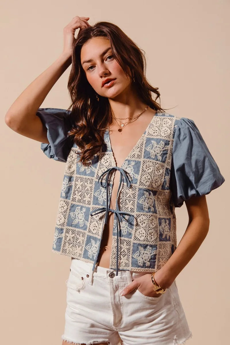 Woman wearing a patterned top with denim sleeves against a beige background