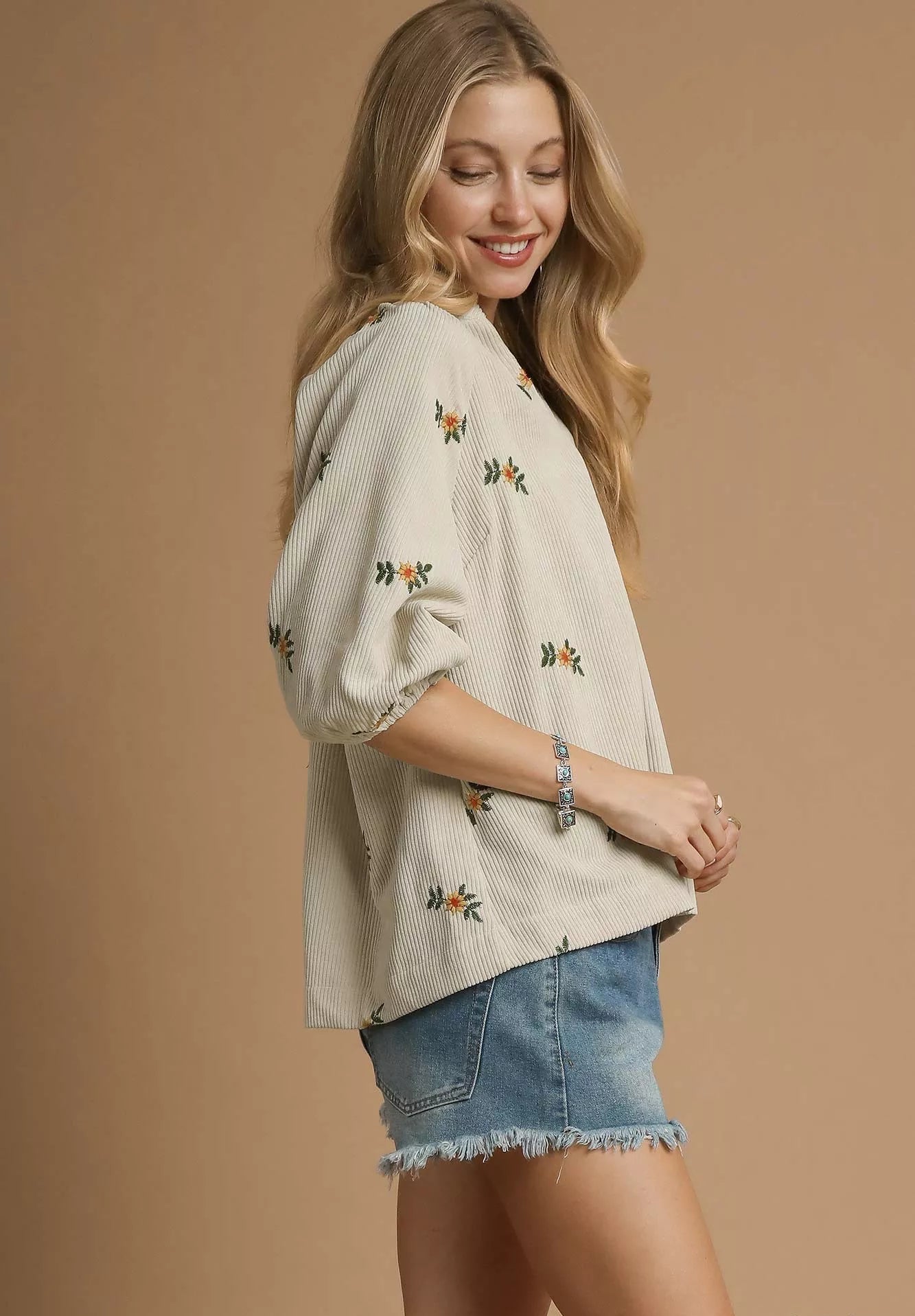 Woman wearing a cream-colored embroidered top and denim shorts on a beige background